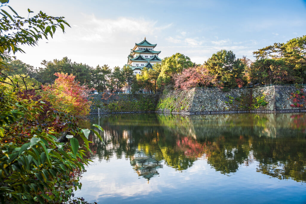 Nagoya Castle rising above its stone walls and moat, framed by autumn foliage and reflected in the water