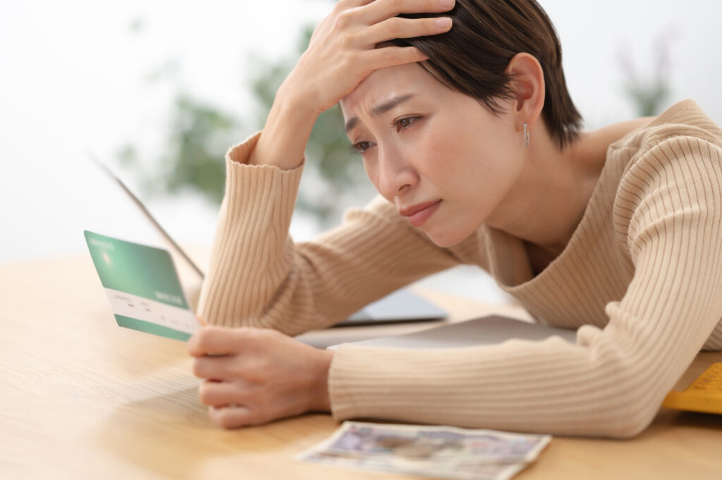 A worried woman rests her head on her hand while looking at a bank passbook, cash on the table