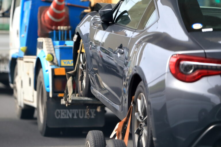 A damaged grey car being loaded onto a blue tow truck on a road after a collision