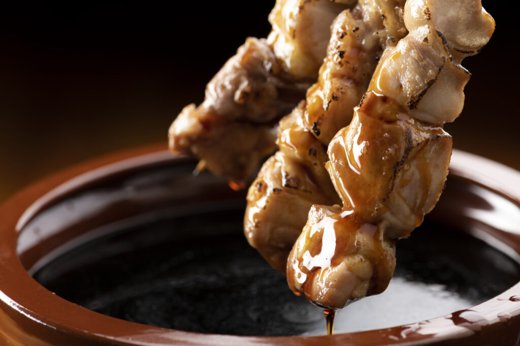 Tare-glazed grilled chicken skewers being lifted from a pot of tare sauce.
