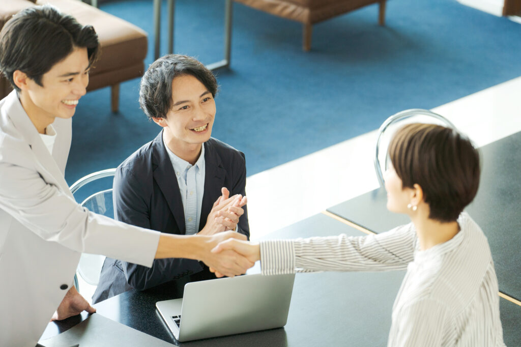Business people smile and shake hands over a laptop at an office table