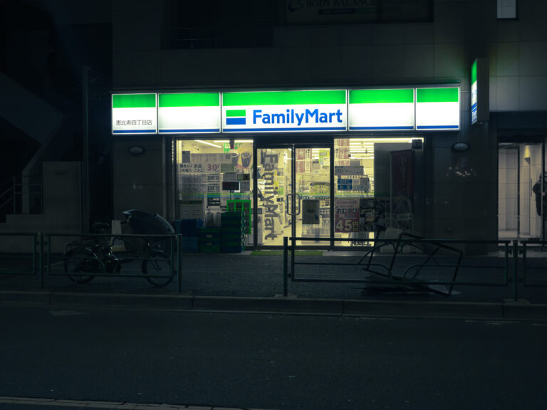 A brightly lit FamilyMart convenience store storefront at night, with bicycles parked on the street outside