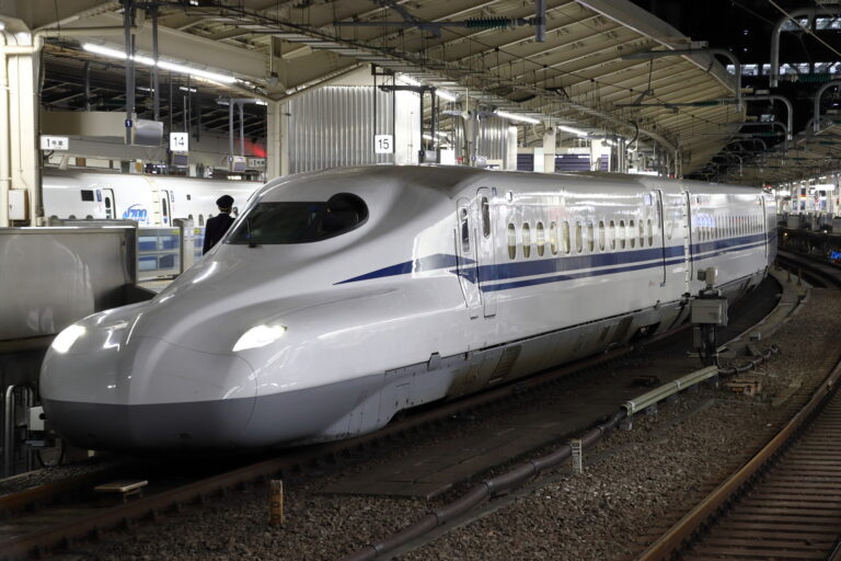 An N700 series Tokaido Shinkansen at a Tokyo Station platform at night, with a crew member standing beside the open cab door.