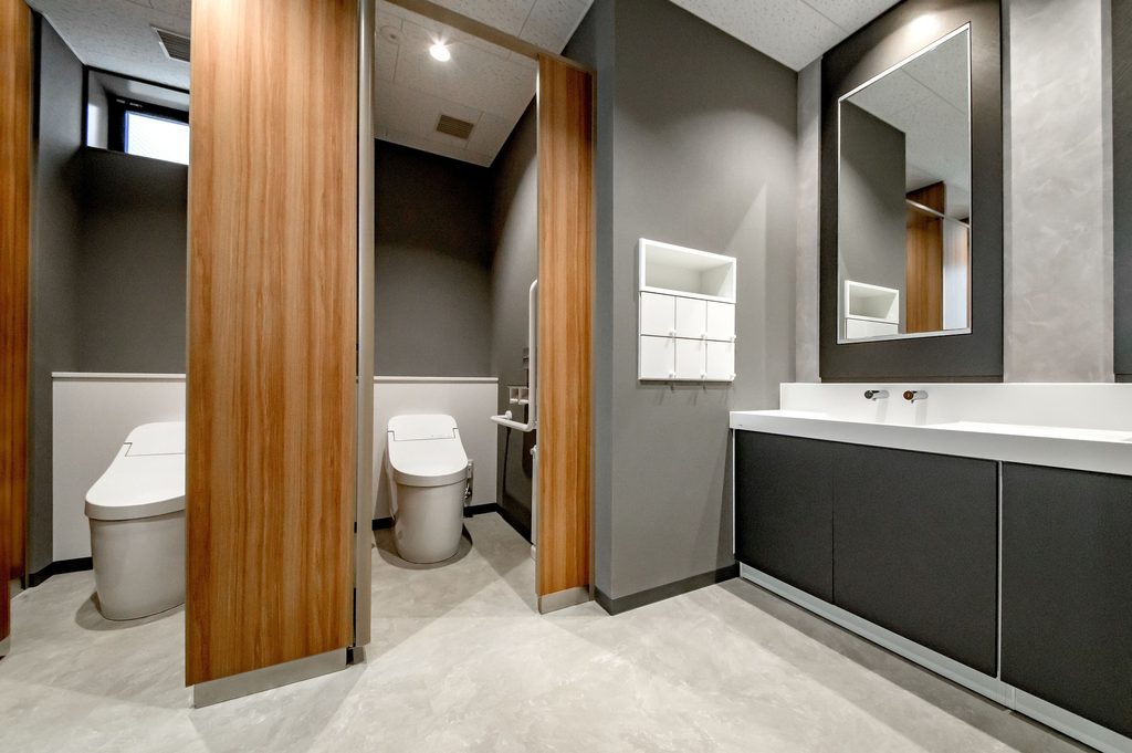 A modern Japanese public restroom with two wood-doored stalls, washlet toilets, and a mirrored vanity.