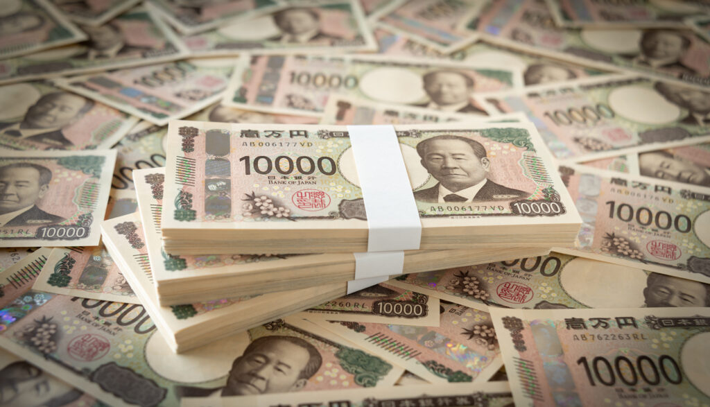 Banded stacks of Japanese 10,000 yen notes resting on a scattered pile of more 10,000 yen notes.