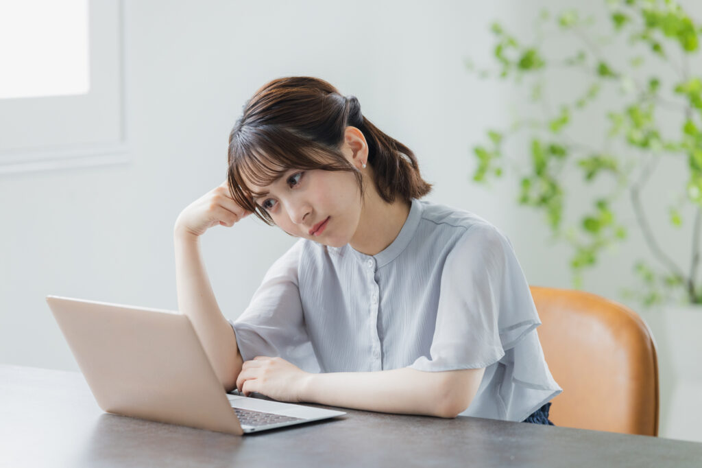 A woman rests her head on her hand while looking at an open laptop