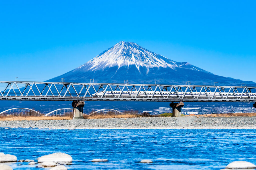 A Shinkansen bullet train crosses a bridge with Mt. Fuji in the background