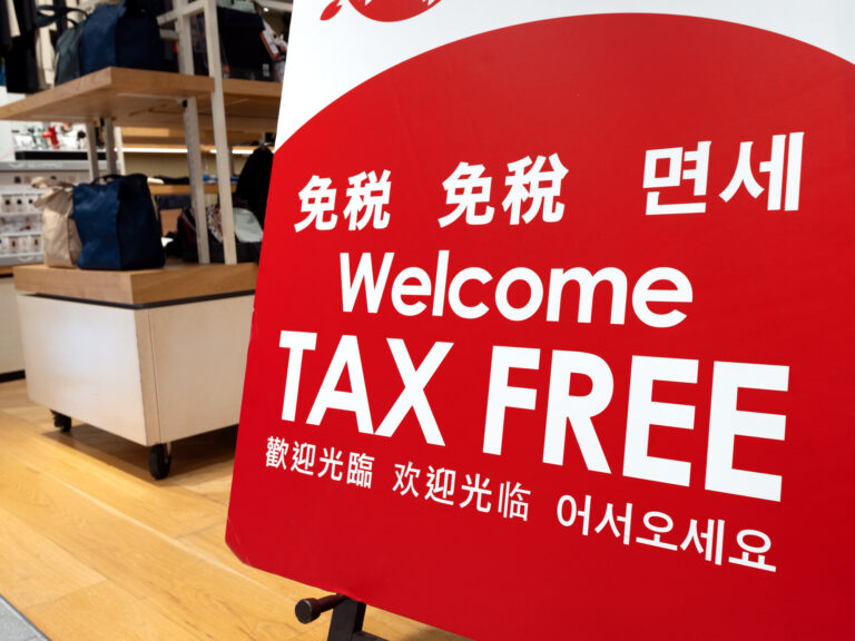 Red and white "Welcome TAX FREE" sign in Japanese, Korean and Chinese, standing on the floor of a Japanese store