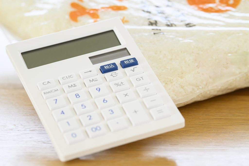 A calculator with tax-included and tax-excluded keys resting on a clear plastic bag of milled white rice.