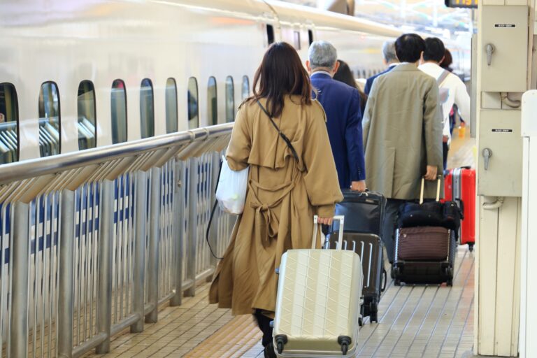 Passengers pulling rolling suitcases board a Shinkansen at a station platform