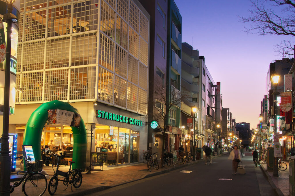 A Starbucks storefront and shopping street in Hiroo, Tokyo, lit up at dusk with bicycles parked along the sidewalk.