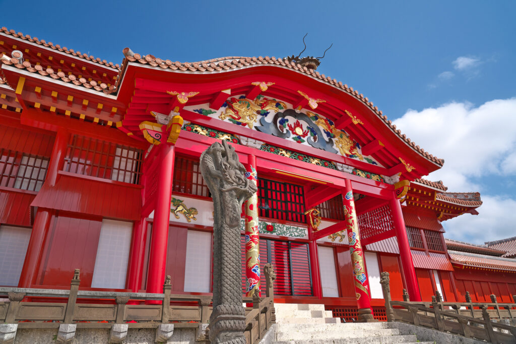 A stone dragon pillar before Shuri Castle's main hall, under the red-and-gold gable with its painted dragon carvings