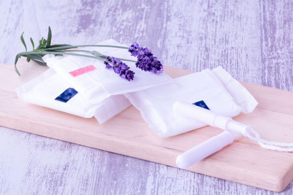 Sanitary pads and tampons displayed on a wooden board with lavender sprigs