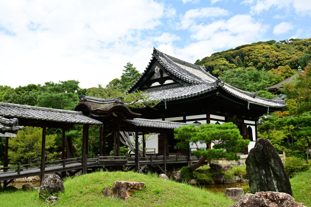 Wooden temple hall with a tiled roof at Kōdai-ji in Kyoto, linked by a covered walkway above a garden of pines and rocks