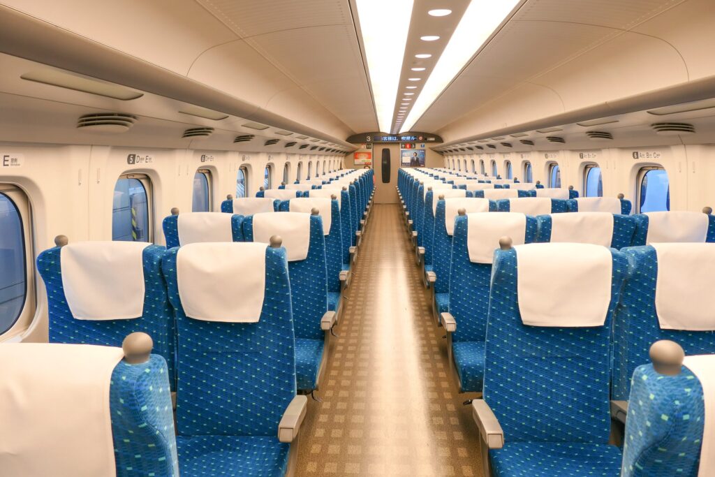 Looking down the aisle of a Tokaido Shinkansen N700A ordinary car. Two seats, D and E, run along the left side and three seats, A, B and C, along the right, with overhead markers labelling each seat letter as window, middle or aisle.