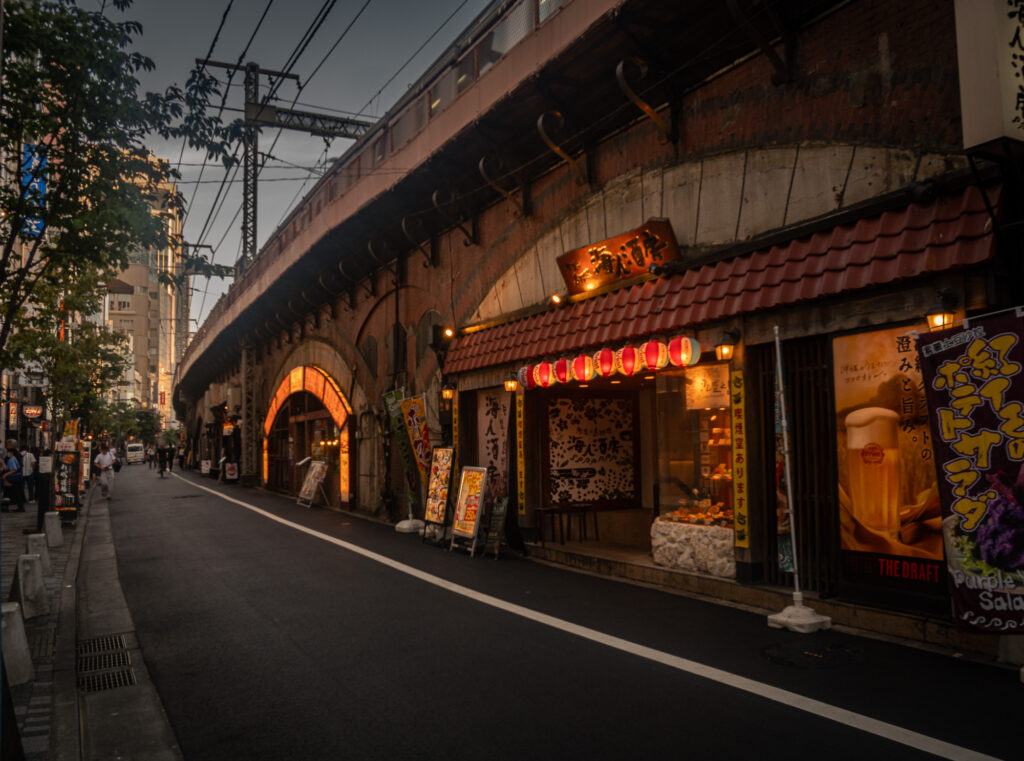 Small storefronts and lanterns along a Yurakucho side street under the tracks