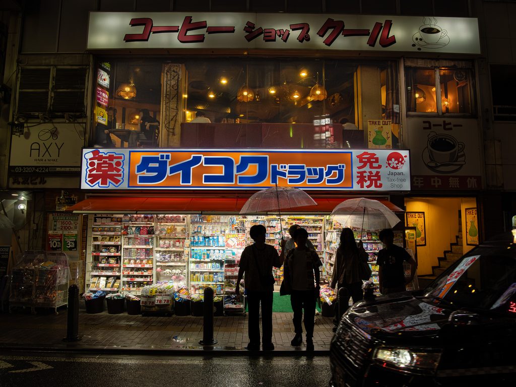 Coffee Shop Cool's lit second-floor windows at night, above a far brighter Daikoku Drug storefront on a rainy street.