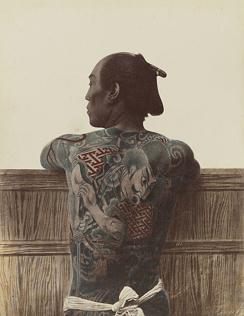 Hand-colored Meiji-era photo of a man seen from behind, his back and arms covered in traditional Japanese tattooing.