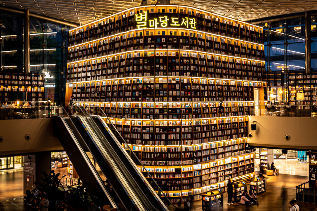 A curved multistory wall of bookshelves under a Hangul sign at Seoul's Starfield Library.