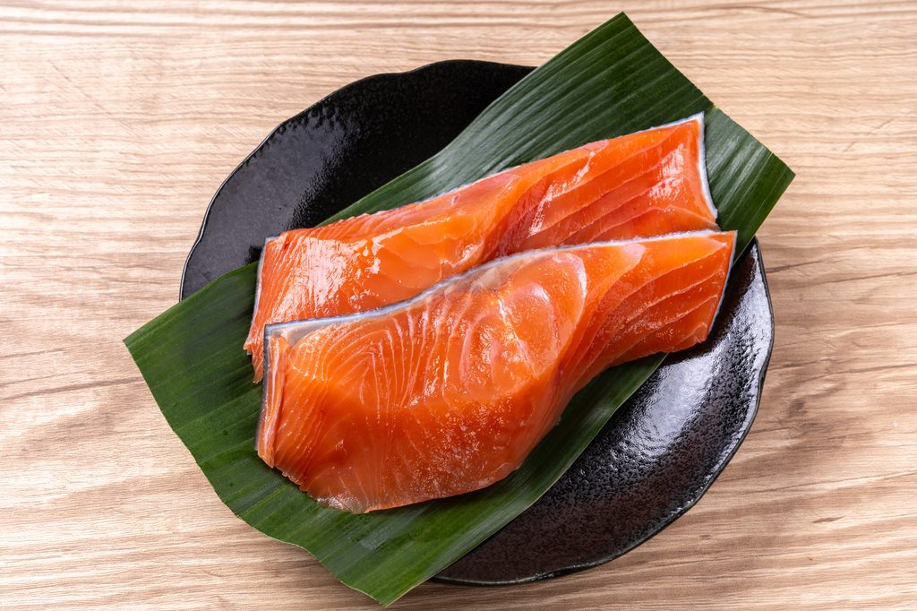 Two raw salmon fillets on a green leaf on a black ceramic plate