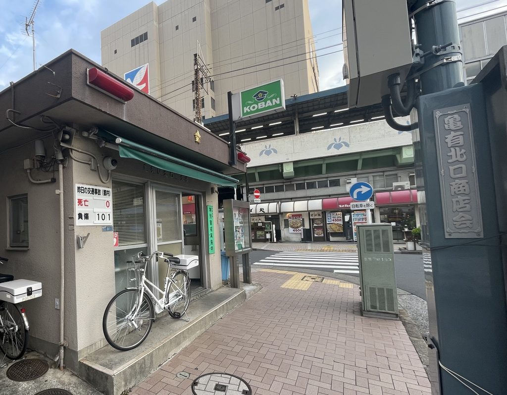 A neighborhood police box with an illuminated KOBAN sign and a police bicycle parked outside, on a street corner.