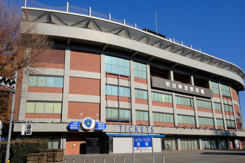 The ticket-gate facade of Meiji Jingu Stadium under a clear blue sky, with its name in kanji on the upper wall.