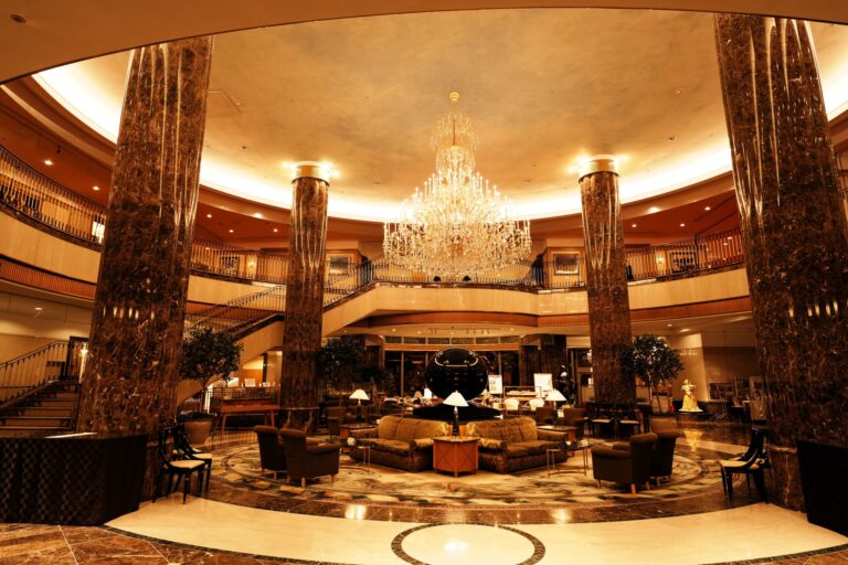 Grand hotel lobby with a large crystal chandelier, dark marble columns, and armchairs on a patterned marble floor