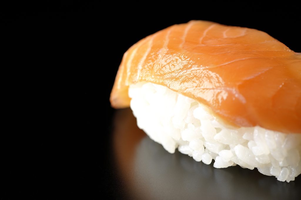 A single piece of salmon nigiri sushi against a black background