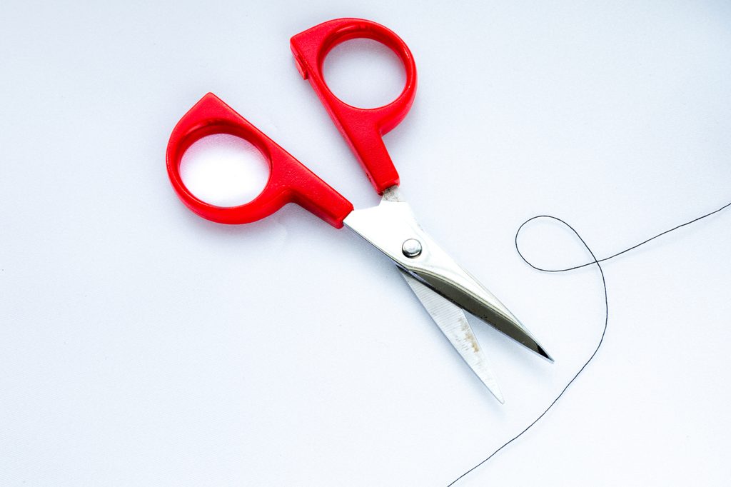 A pair of red-handled scissors beside a loose length of black thread on a white surface