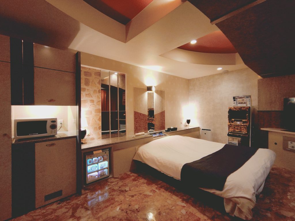 A love hotel guest room with mirrored panels, a marble floor, a bedside control console, microwave and mini-fridge.
