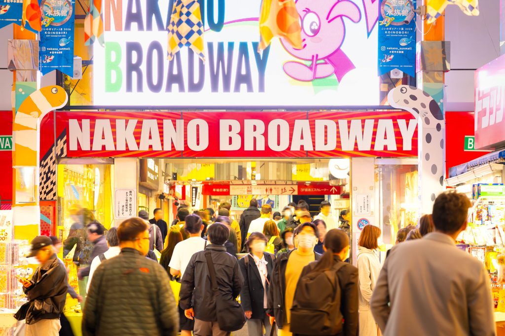 Crowds entering Nakano Broadway at night beneath the shopping complex's illuminated red sign.