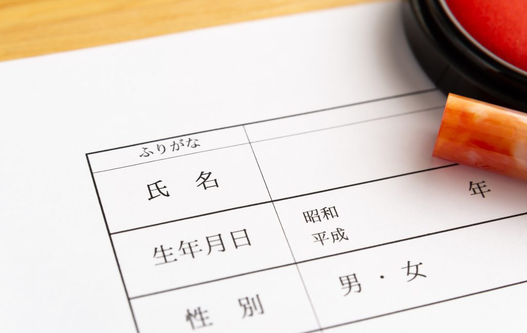 Japanese form with fields for name and its furigana, date of birth, and sex, next to a hanko seal and red ink pad
