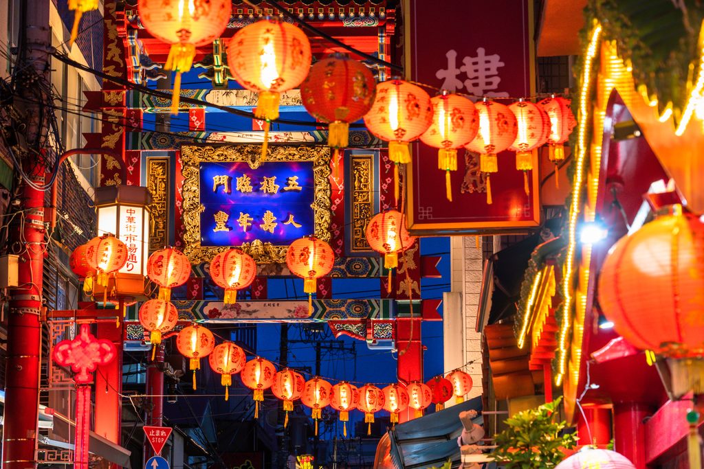 Red paper lanterns strung along Market Street in Yokohama Chinatown at night, beneath its ornate gate.