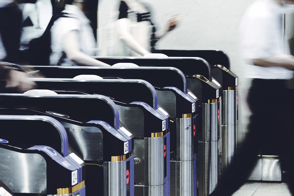 A row of automatic ticket gates at a Japanese railway station, with commuters passing through in motion blur.