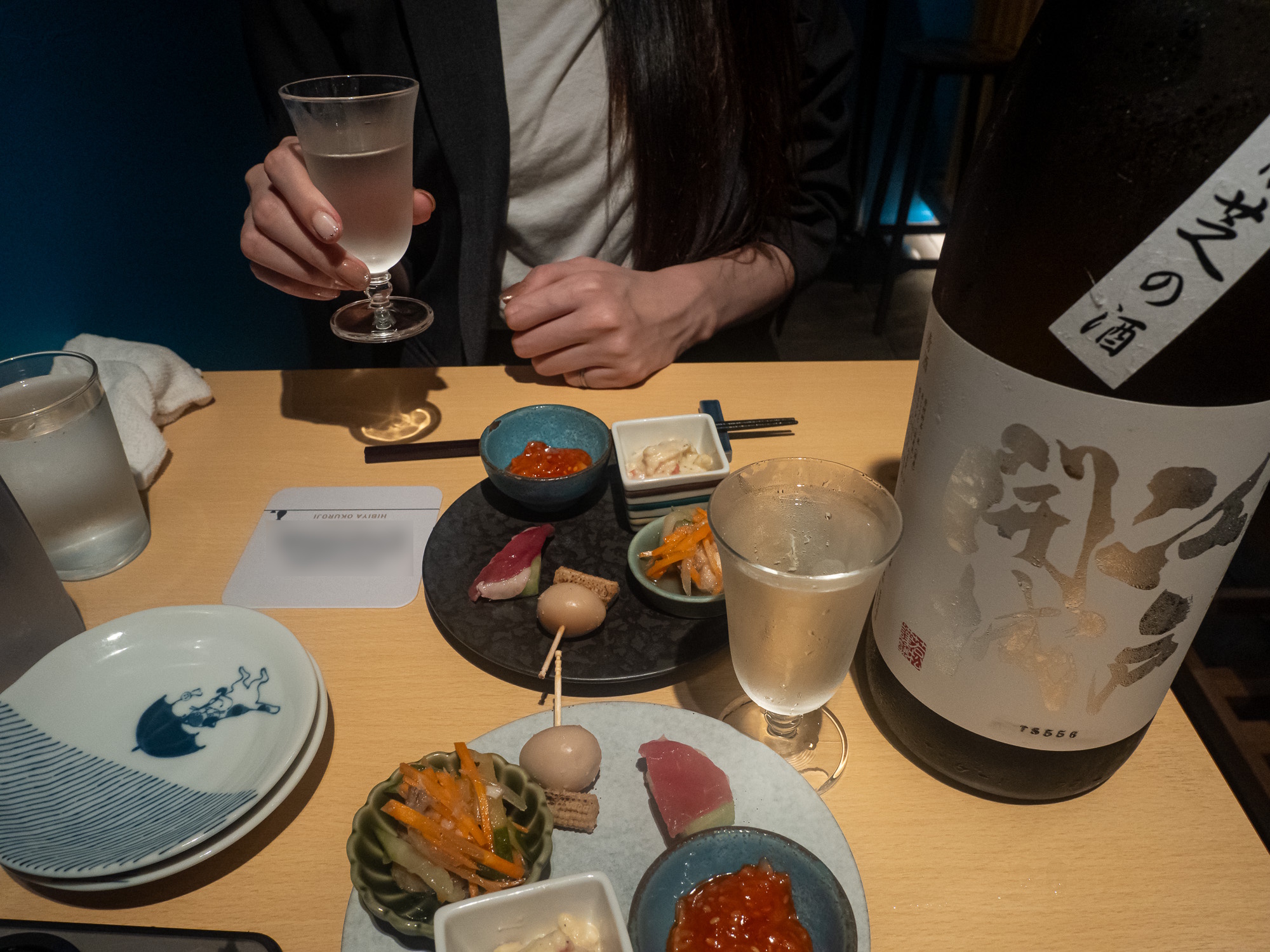 A guest raising a glass of sake at a table set with small dishes