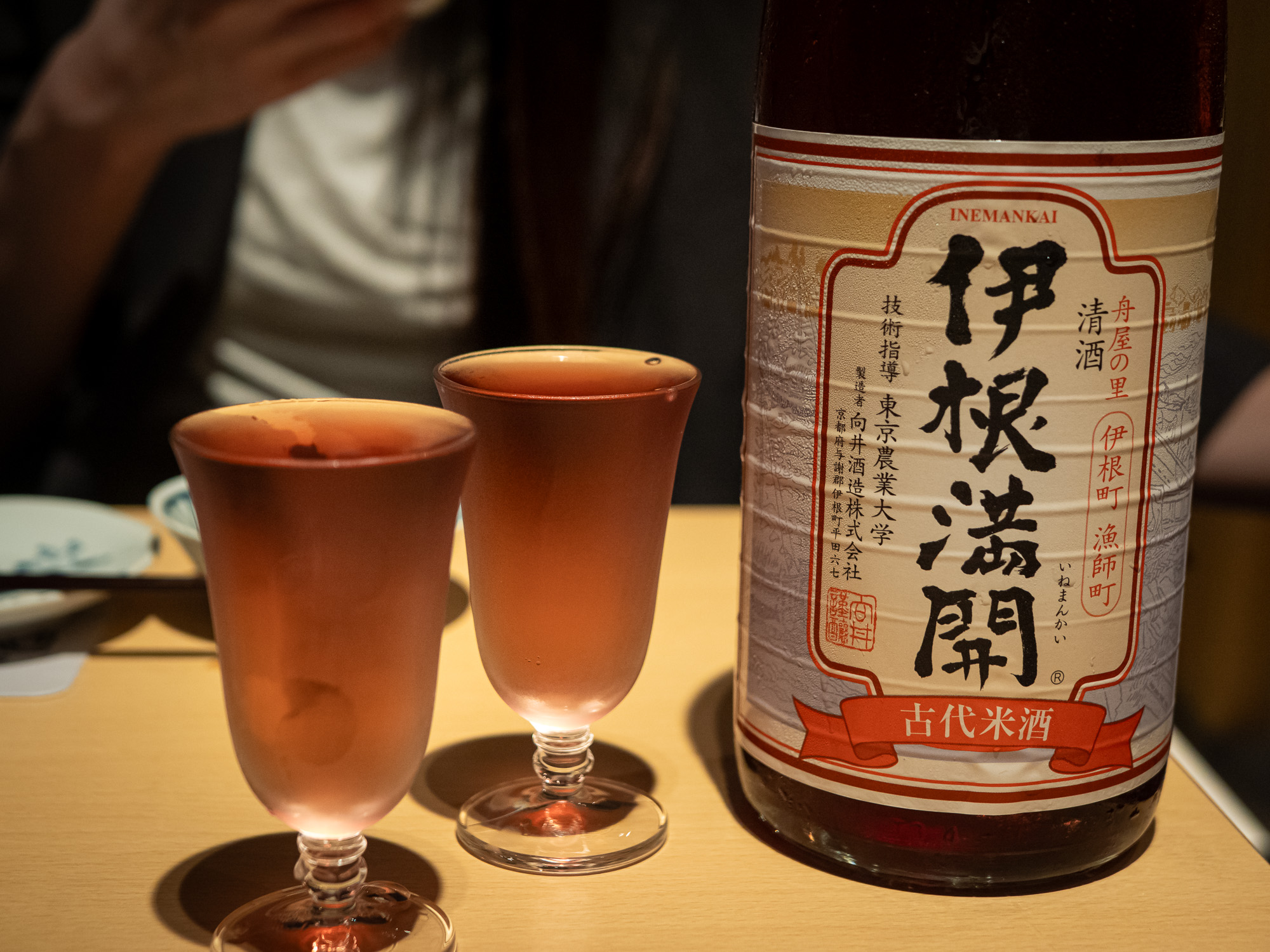 Two glasses of Inemankai, a pink ancient-rice sake, standing beside the bottle