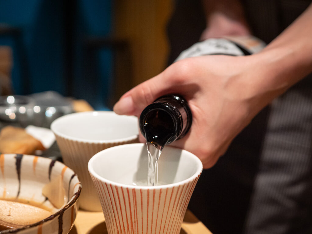 Sake being poured from a dark bottle into a small ceramic cup