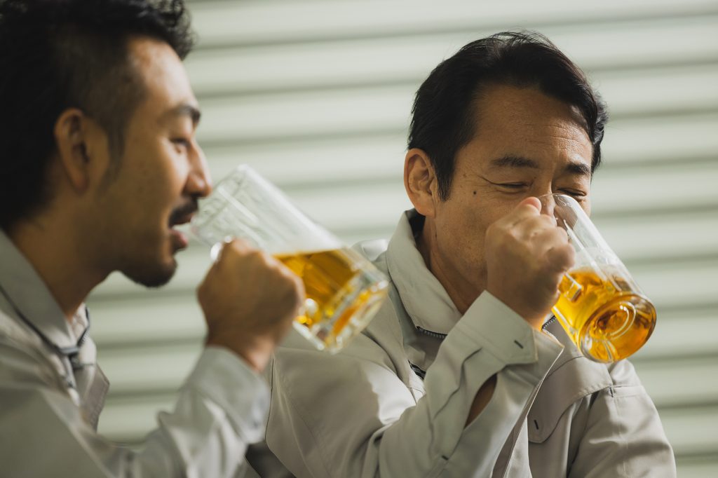 Two Japanese men in gray work jackets drinking from beer mugs