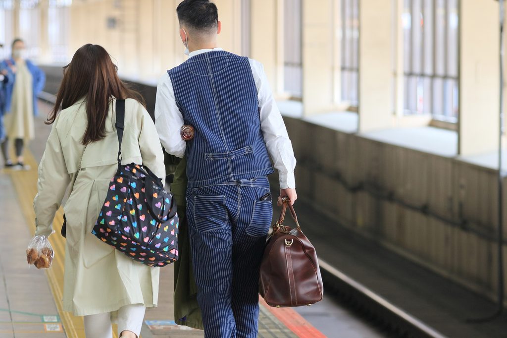 Man in a pinstriped vest walking shoulder to shoulder with a woman carrying a heart-print bag on a train platform