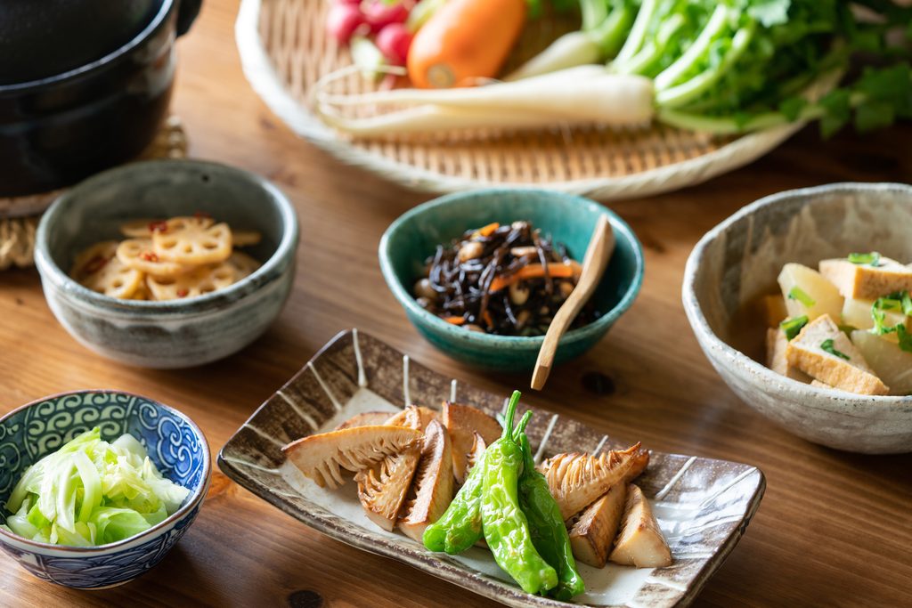 Small Japanese vegetable side dishes: lotus root, hijiki seaweed, grilled bamboo shoots with green peppers, simmered tofu, and pickled cabbage.