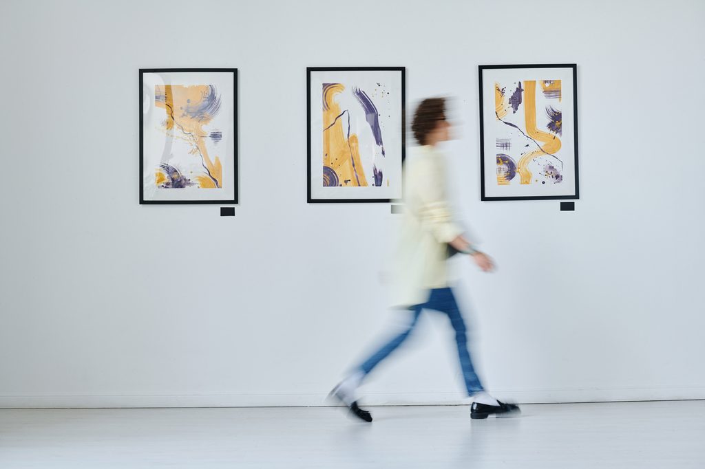 A visitor walks past three framed abstract paintings hung on a white gallery wall