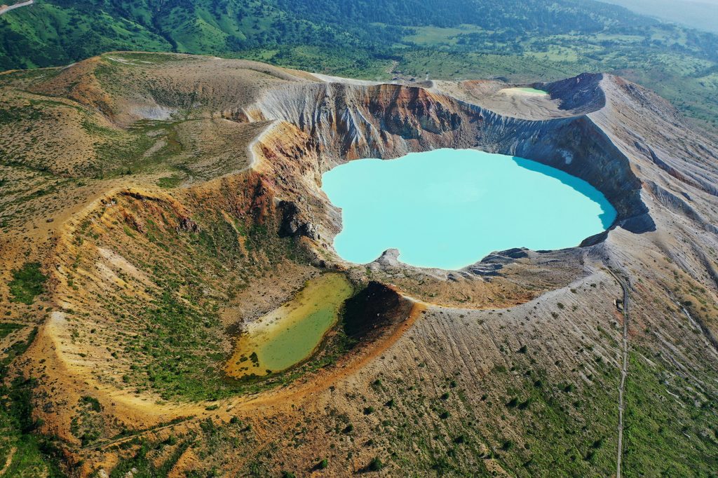 Aerial view of Yugama's turquoise crater lake, with a smaller green crater pond beside it